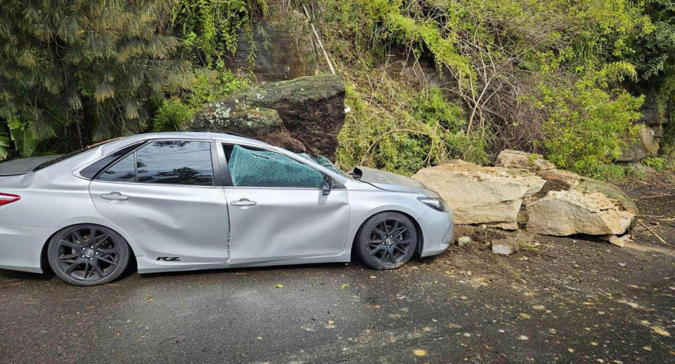 Silver sedan car parked on side of Whale Beach Road, Palm Beach after a large slab of sandstone fell on top of it during a landslide. 
