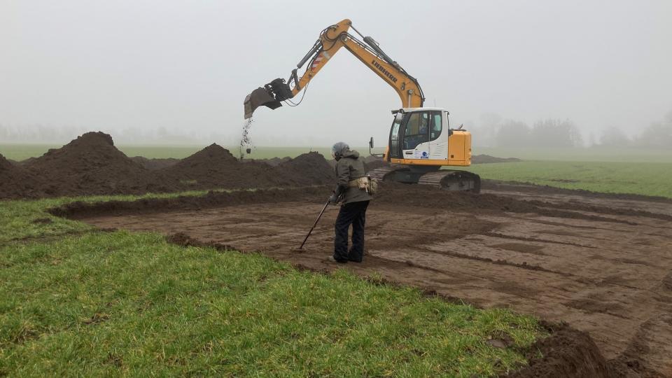 The silver was found late last year on a farm near the town of Hobro in the north of Jutland by a metal detectorist with a local archaeology group. Here we see a large yellow digger dredging up dirt in a field. There is also another person scanning the recently upended earth.