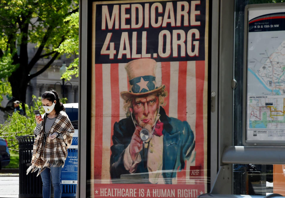 A pedestrian wearing a protective mask checks her phone near a Medicare for All bus stop billboard in Washington, DC.