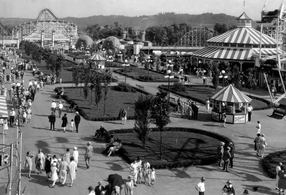 MAY 1928: Coney Island. Spotting straw hats, suits and dresses, fun-seekers stroll the mall at Coney island. Roller-coaster cars climb distant tracks as the Ferris wheel pauses between rides. Many of these visitors came to the park aboard the "Island Queen."