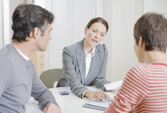 A woman in business attire reviews a document with a couple across the desk.