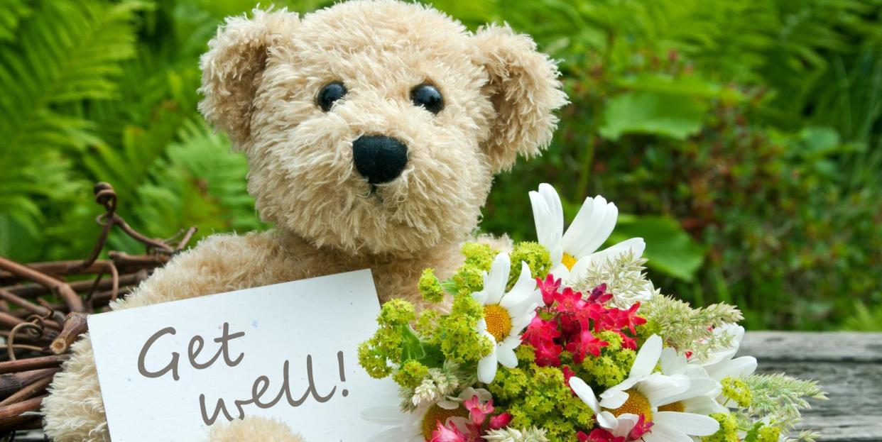 teddy bear with white and red flowers and card with a message that reads get well