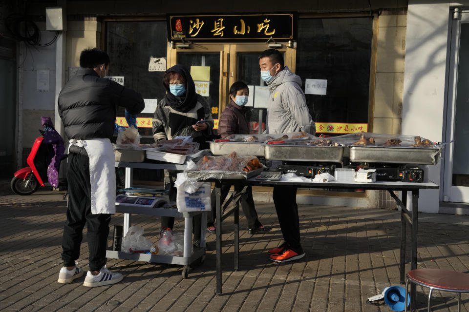 Residents buy cooked food from a vendor selling on the street after restaurants were order closed in Beijing, Friday, Nov. 25, 2022. Residents of China's capital were emptying supermarket shelves and overwhelming delivery apps Friday as the city government ordered accelerated construction of COVID-19 quarantine centers and field hospitals. (AP Photo/Ng Han Guan)