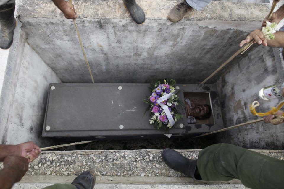 In this Feb. 5, 2014 photo, Divaldo Aguiar, who plays the part of Pachencho, is lowered inside a grave site as he lies inside a mock coffin as part of the Burial of Pachencho celebration at a cemetery in Santiago de Las Vegas, Cuba. A man masquerading as a priest makes the sign of the cross over the grave and mutteres, "rest in peace." People blow trumpets, bang drums and toss flowers. Then villagers splash rum into Aguiar's mouth from above, and he opens his eyes and climbs out of the tomb."Being reborn is the most beautiful thing there is in life," said Aguiar, who said he has played "Pachencho” for several years running. (AP Photo/Franklin Reyes)