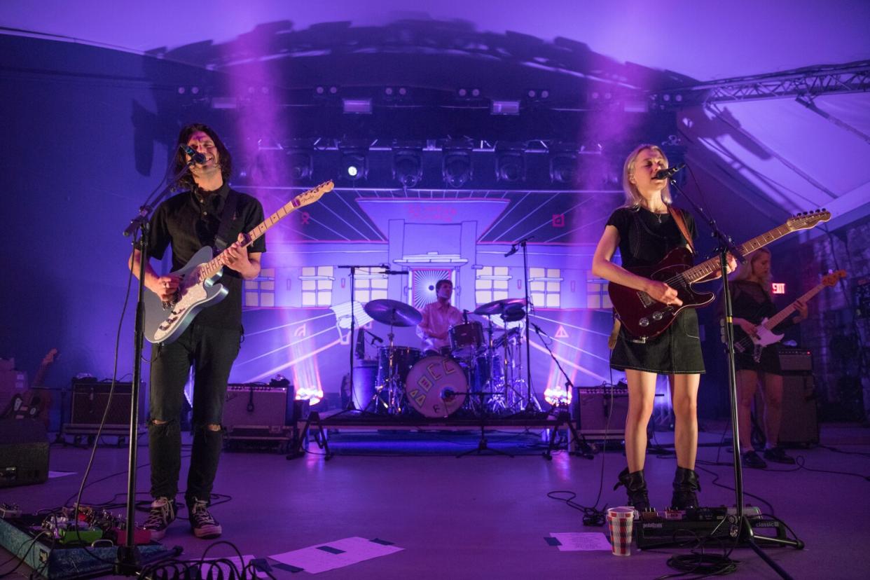 A man and a woman, both playing electric guitar and singing, onstage.