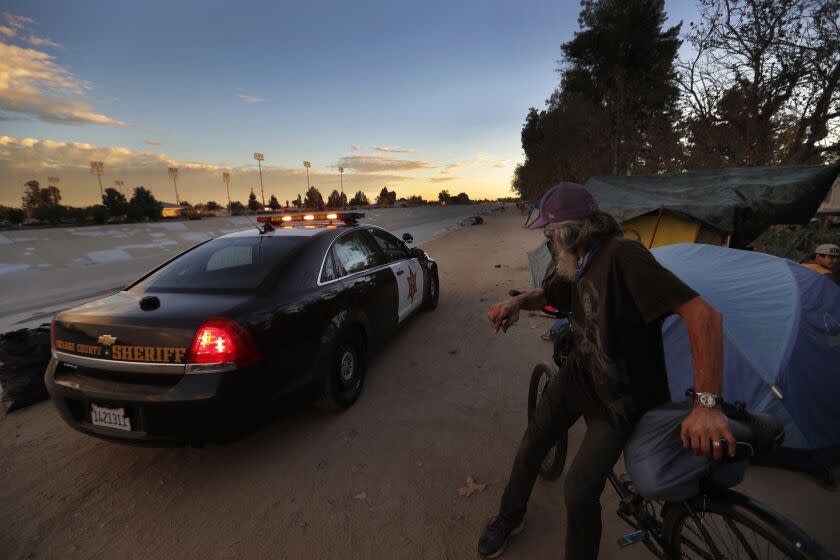 Greg Schulz, who has been homeless for a year, watches an Orange County Sheriff cruiser patrol the Santa Ana River bed