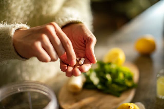 <p>vorDa / Getty Images</p> Taking a supplement in the kitchen close up