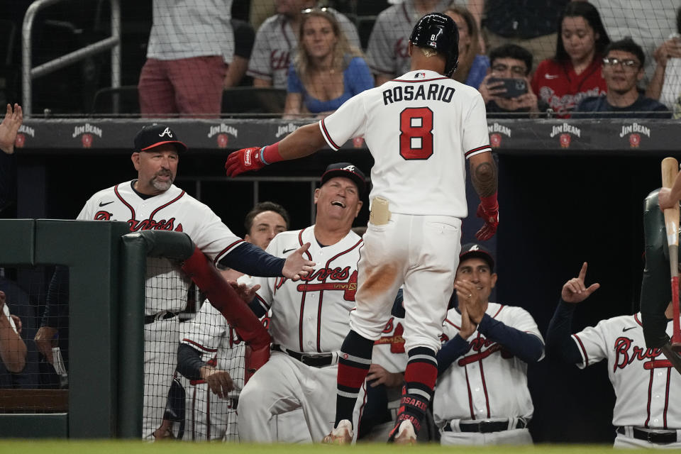 Atlanta Braves' Eddie Rosario (8) is greeted at the dugout by bench coach Walt Weiss, left, and manager Brian Snitker after hitting a solo home run against the Cincinnati Reds during the eighth inning of a baseball game Wednesday, April 12, 2023, in Atlanta. (AP Photo/John Bazemore)