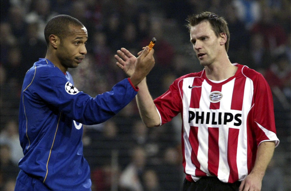 FILE - Andre Ooijer of PSV, right, gestures as Thierry Henry of Arsenal holds a lighter that was thrown on the pitch during the UEFA Champions League soccer match between PSV Eindhoven and Arsenal at the Philips stadium in Eindhoven, The Netherlands, Wednesday Nov 24, 2004. (AP Photo/Fred Ernst, File)