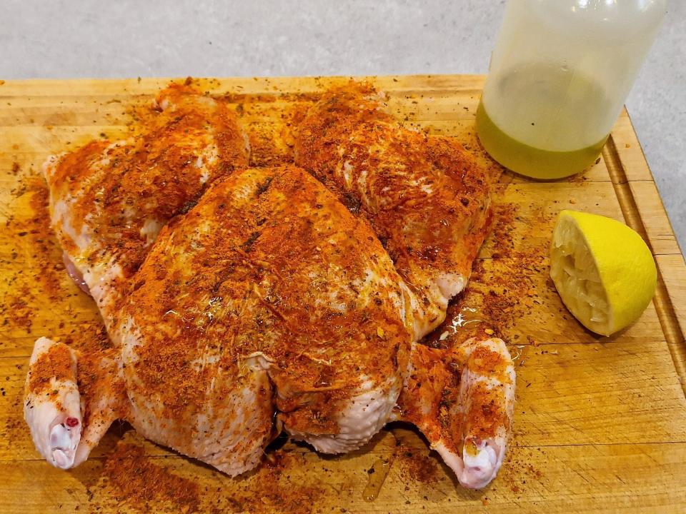 seasoned spatchcocked chicken on a cutting board with half a lemon and a bottle of oil