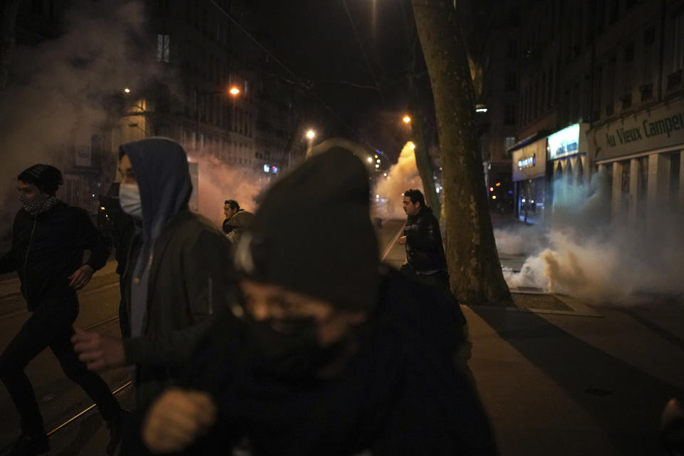 Protesters run in tear gas through the streets of Lyon, central France, after parliament adopted a divisive pension bill, Monday, March 20, 2023. The French government has survived two no-confidence votes in the lower chamber of parliament, proposed by lawmakers who objected to its push to raise the retirement age from 62 to 64. (AP Photo/Laurent Cipriani)