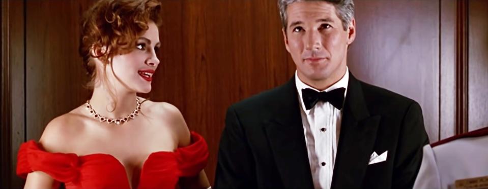 Julia Roberts looking at Richard Gere with an amused expression during a scene from "Pretty Woman" where they ride together in an elevator on their way to their seats at the opera.