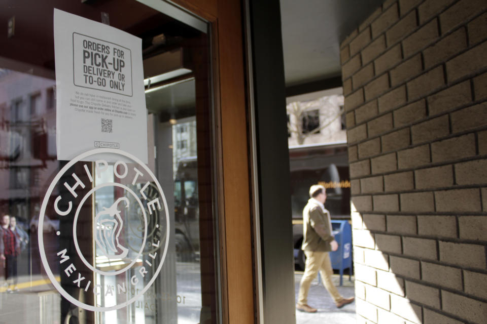 A sign indicating that only carry-out or delivery options are available hangs in the window of a closed Chipotle restaurant in Portland, Ore., Monday, March 16, 2020. Gov. Kate Brown announced a four-week ban on eat-in dining at bars and restaurants throughout the state on Monday to slow the spread of the new coronavirus in Oregon. Restaurants can still offer take-out and delivery. (AP Photo/Gillian Flaccus)