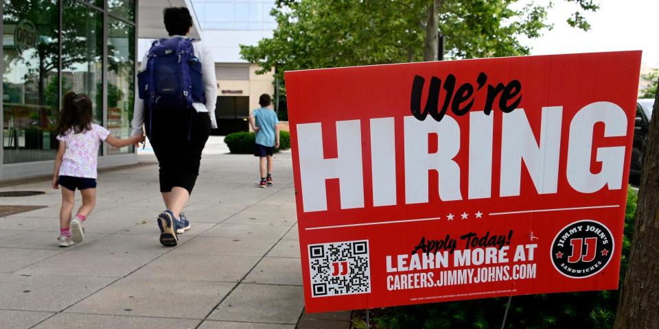 People walk past a "We're Hiring" sign at a Jimmy John's.