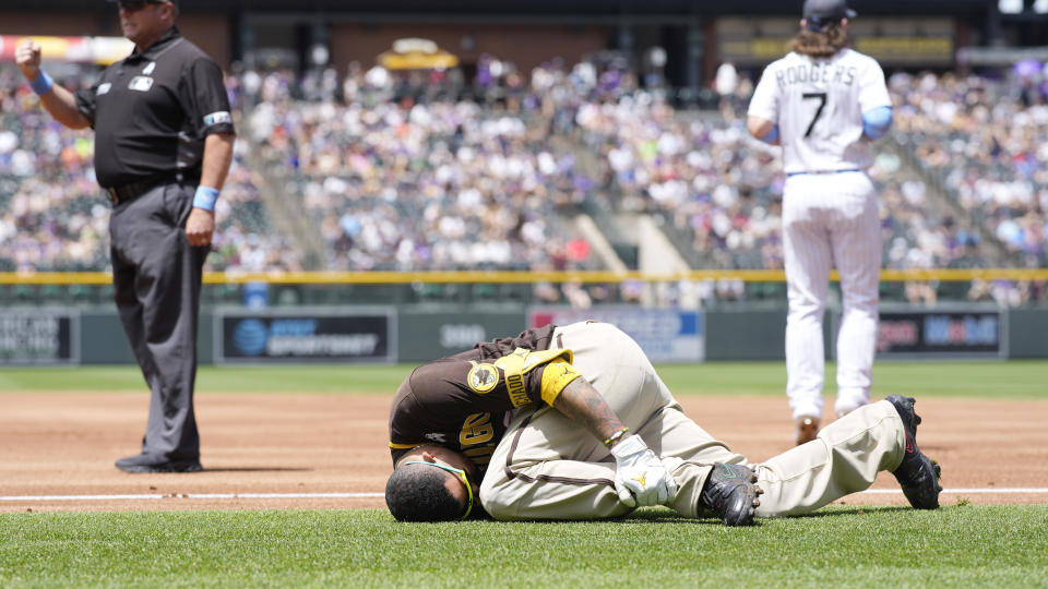 San Diego Padres' Manny Machado grips his left ankle after falling over first base while trying to beat out an infield hit to Colorado Rockies starting pitcher Antonio Senzatela in the first inning of a baseball game, Sunday, June 19, 2022, in Denver. Machado was helped off the field and was called out on the play. (AP Photo/David Zalubowski)