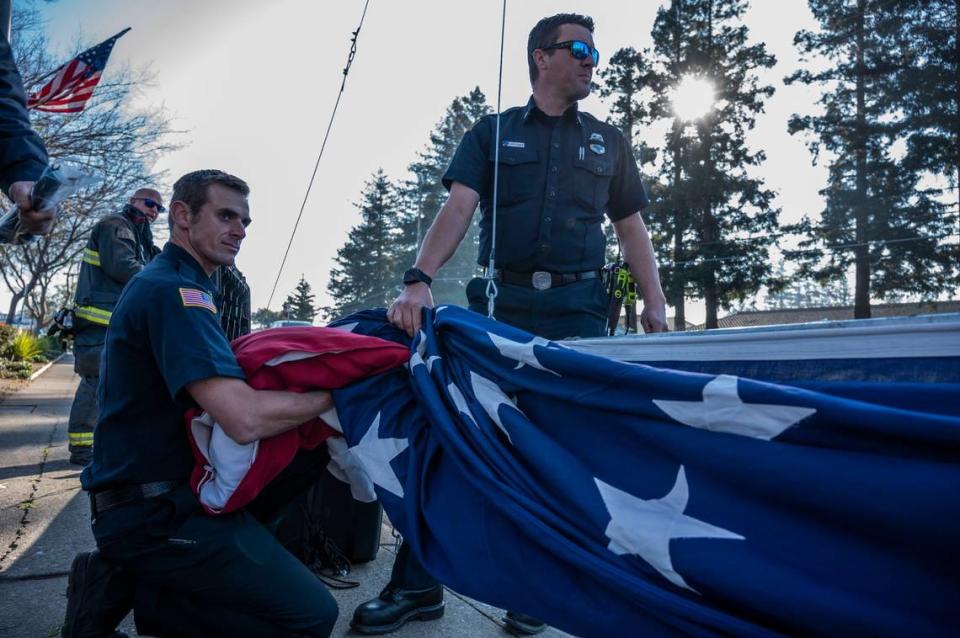 Members of the Cosumnes Fire Department help raise a flag on Elk Grove Boulevard as they prepare for a procession for fallen Elk Grove police officer Ty Lenehan on Tuesday, Jan. 25, 2022. Lenehan died after he collided with a wrong way driver on his way to work early Friday morning in Sacramento on Jan. 21.