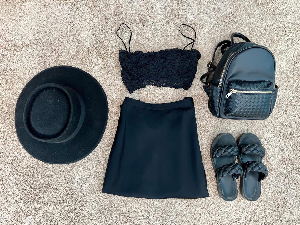 Black sandals, black backpack, black wide-brimmed hat, and black two-piece dress spread out on floor.