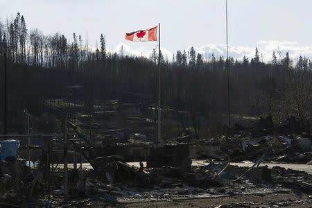 A Canadian flag flies over damage caused by a wildfire, which prompted the mass evacuation of over 88,000 people, in Fort McMurray, Alberta, Canada on May 14, 2016. Chris Schwarz/Government of Alberta/Handout via REUTERS