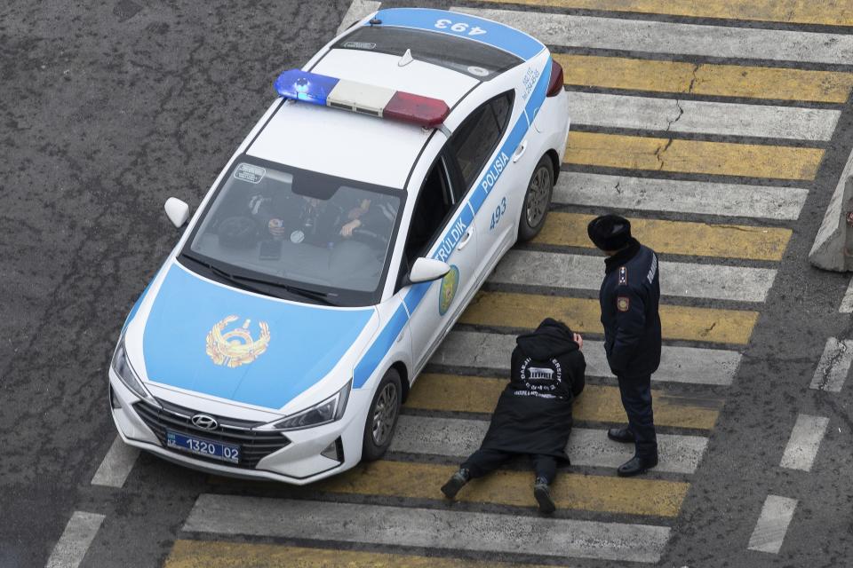 A police officer watches over a man as his papers are checked by colleagues at a crossing, on a street in Almaty, Kazakhstan, Monday, Jan. 10, 2022. Life in Almaty, which was affected with the violence the most during protests, started returning to normal this week, with public transport resuming operation and malls reopening. (AP Photo/Vasily Krestyaninov)