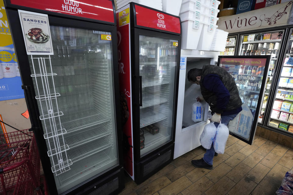 Kevin Savaya, manager at Mr. C's Deli, carries bags of ice past empty coolers in Grosse Pointe Farms, Mich., Friday, Feb. 24, 2023. The business was staying open using a generator. Michigan is shivering through extended power outages caused by one of the worst ice storms in decades. (AP Photo/Paul Sancya)