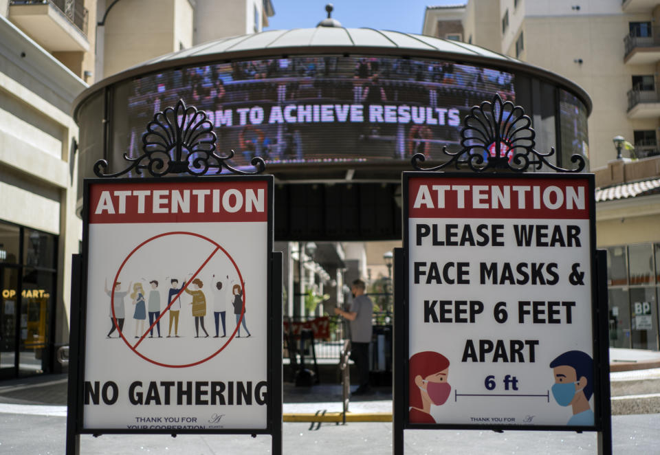 FILE - In this June 11, 2021, file photo, signs with social distancing guidelines and face mask requirements are posted at an outdoor mall amid the COVID-19 pandemic in Los Angeles. Businesses large and small are reinstituting mask mandates and requiring vaccines of their customers as U.S. coronavirus cases rise. (AP Photo/Damian Dovarganes, File)