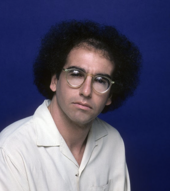 Young Larry David with a black curly hair and glasses