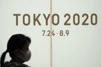 A woman walks past a large display promoting the Tokyo 2020 Olympics in Tokyo, Friday, March 13, 2020. U.S. President Donald Trump's suggestion to postpone the Tokyo Olympics for a year because of the spreading coronavirus was immediately shot down by Japan's Olympic minister. For most people, the new coronavirus causes only mild or moderate symptoms. For some it can cause more severe illness. (AP Photo/Jae C. Hong)