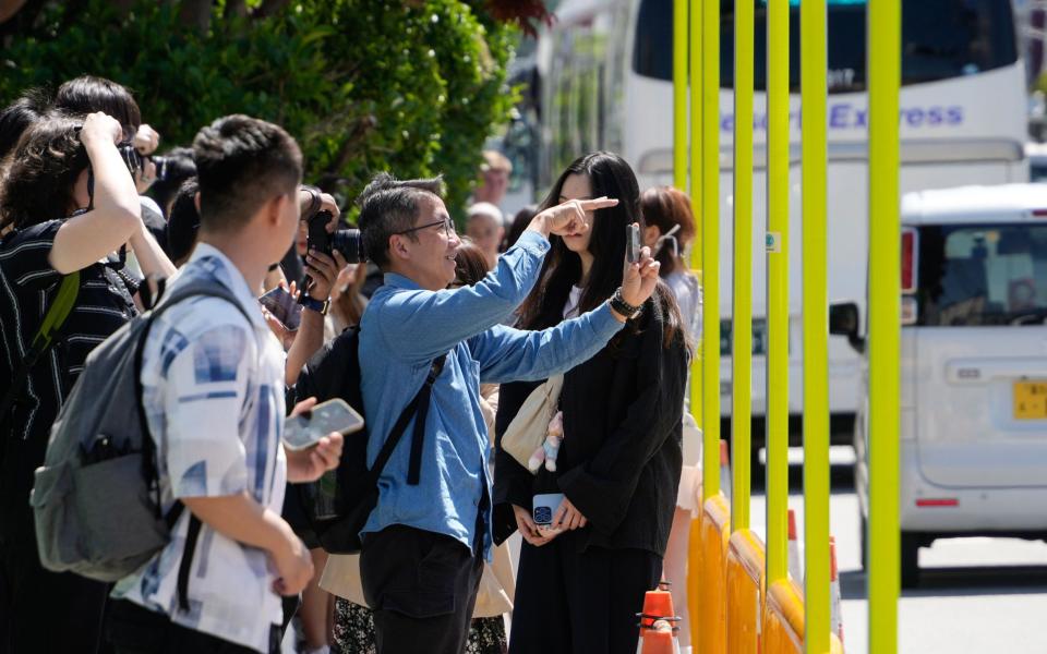 Tourists pictured behind the barrier's metal bars in Fujikawaguchiko. The black curtain will be installed in the second half of May