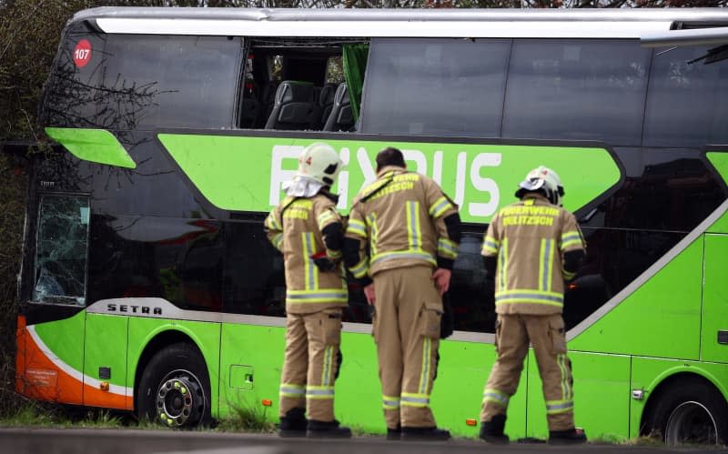 Three firefighters stand in front of a coach at the scene of an accident on the A9. At least five people died and several were injured in an accident involving a coach on the A9 near Leipzig. Jan Woitas/dpa