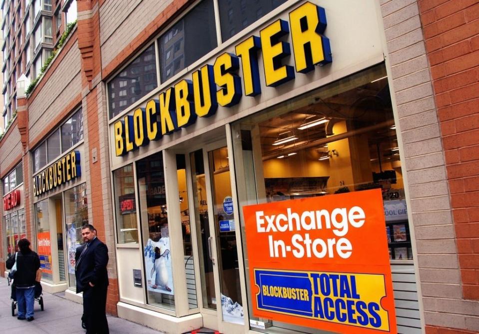 Blockbuster storefront with "Exchange In-Store" sign. A man stands outside, reflecting on the iconic brand's role in the history of retail entertainment