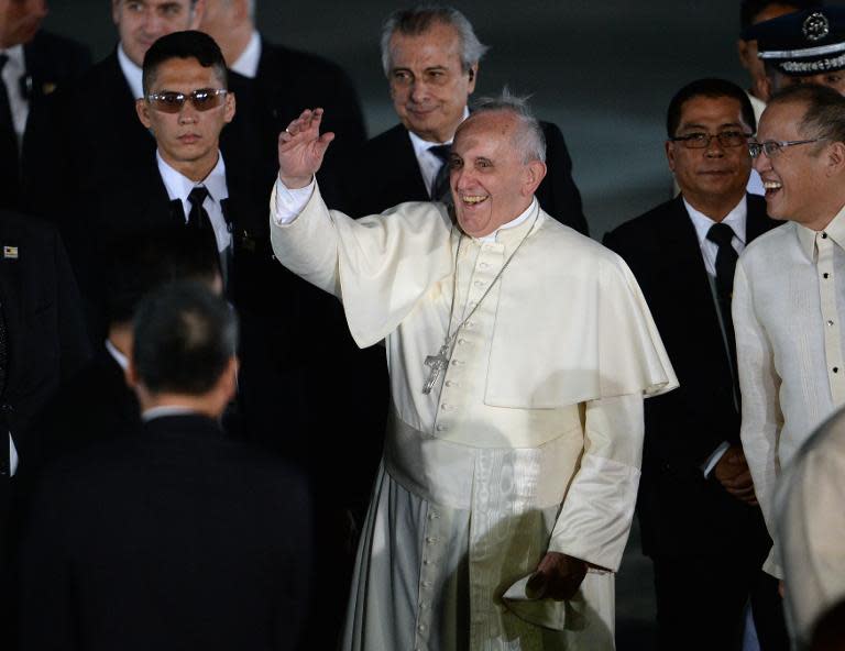 Pope Francis waves to students delivering a performance shortly after arriving at a military airbase in Manila on January 15, 2015, where he was greeted by President benigno Aquino (R)