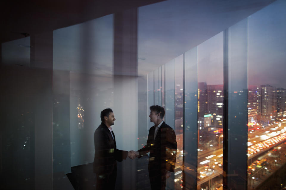 Businessmen shaking hands in conference meeting room in contemporary modern office at night