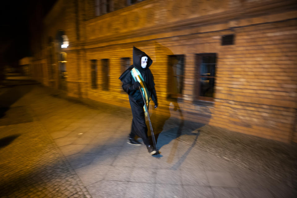 Brazilian activist and artist Rafael Puetter, dressed as the grim reaper, walks in a one-man protest through Berlin, Germany, early Wednesday, April 7, 2021. The multimedia artist starts his performance at the Brazilian embassy in Berlin at midnight every night to protest against Brazil's COVID-19 policies. Rafael Puetter walks to the Brandenburg Gate and then to the nearby German parliament building, in front of which he counts out a sunflower seed to represent each of the lives that were lost over the past 24 hours in Brazil because of the coronavirus pandemic. (AP Photo/Markus Schreiber)