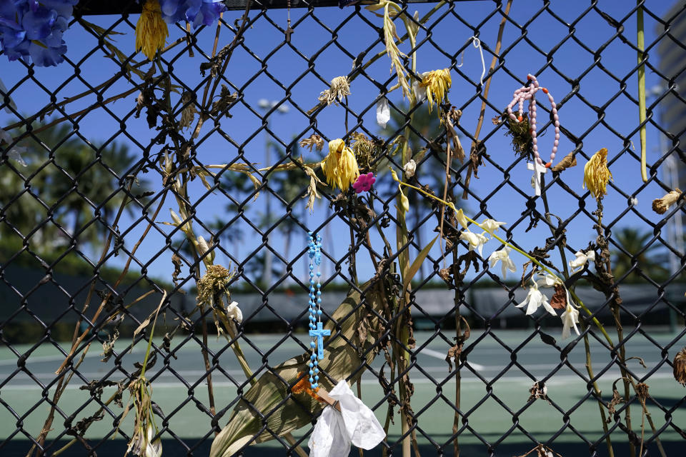 Dried flowers hang from a fence as staff with the HistoryMiami Museum work at the site of a memorial wall honoring the victims of the nearby deadly building collapse on June 24 that killed 98 people, Monday, Aug. 30, 2021, in Surfside, Fla. The museum is working with the city and county to catalog the items and preserve them in an archival bin for safekeeping. (AP Photo/Lynne Sladky)