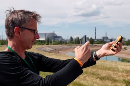 A visitor takes a picture of a dosimeter near the New Safe Confinement (NSC) structure over the old sarcophagus covering the damaged fourth reactor at the Chernobyl Nuclear Power Plant, in Chernobyl