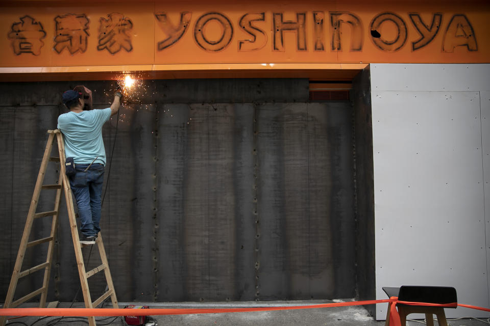 A worker welds metal plates at the entrance of a closed Yoshinoya restaurant in Hong Kong, Friday, Oct. 25, 2019. Banks, retailers, restaurants and travel agents in Hong Kong with ties to mainland China or perceived pro-Beijing ownership have fortified their facades over apparent concern about further damage after protesters trashed numerous businesses following a recent pro-democracy rally. (AP Photo/Mark Schiefelbein)