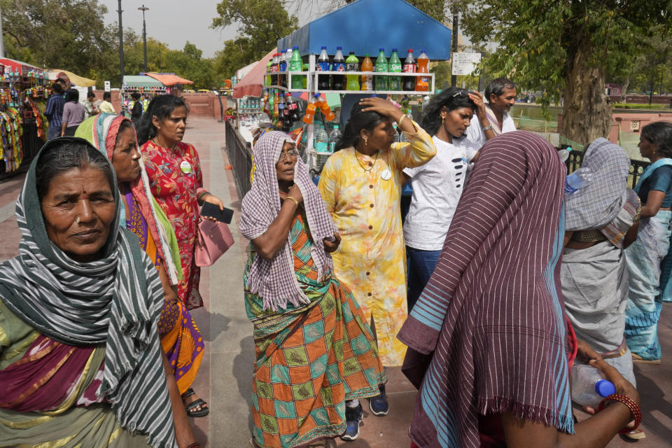 Local tourists cover their heads to shield from the heat as they buy drinking water bottles, in New Delhi, India, Tuesday, June 18, 2024. A monthslong heatwave across swathes of India has killed more than 100 people and led to over 40,000 suspected cases of heat stroke in the last three and a half months, a Health Ministry official said Thursday. (AP Photo/Manish Swarup)