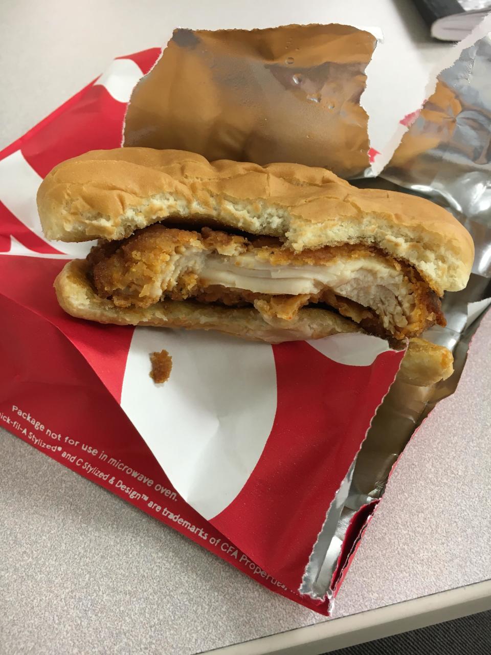 A half-eaten chicken sandwich on open fast-food wrapper