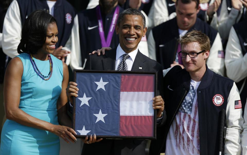 President Barack Obama and first lady Michelle Obama are presented with the U.S. Olympic flag by Navy Veteran Brad Snyder, during a ceremony on the South Lawn of the White House in Washington, Friday, Sept. 14, 2012, welcoming the 2012 U.S. Olympic and Paralympic teams. (AP Photo/Pablo Martinez Monsivais)