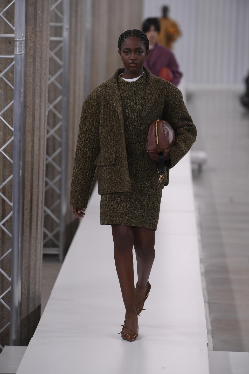 Zaya walks down a long white runway in a short dress and matching jacket