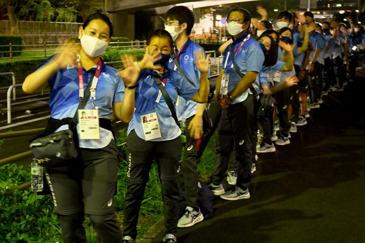 Japanese volunteers wave for visitors as they wait for their bus in front of the the Tokyo Aquatics Centre in Tokyo on July 29, 2021, during the Tokyo 2020 Olympic Games. (Photo by Attila KISBENEDEK / AFP) (Photo by ATTILA KISBENEDEK/AFP via Getty Images)