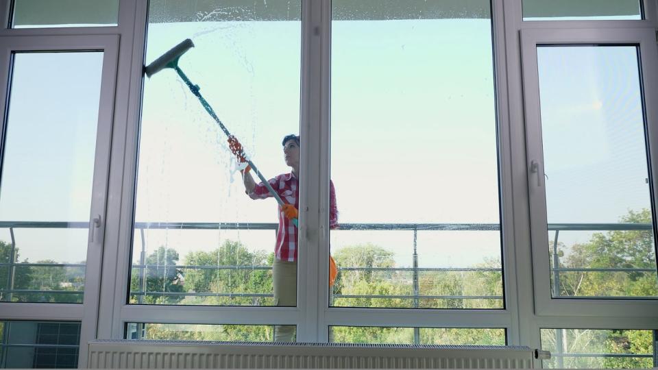 Woman standing outside on a deck using a window wiping tool to tall windows. 