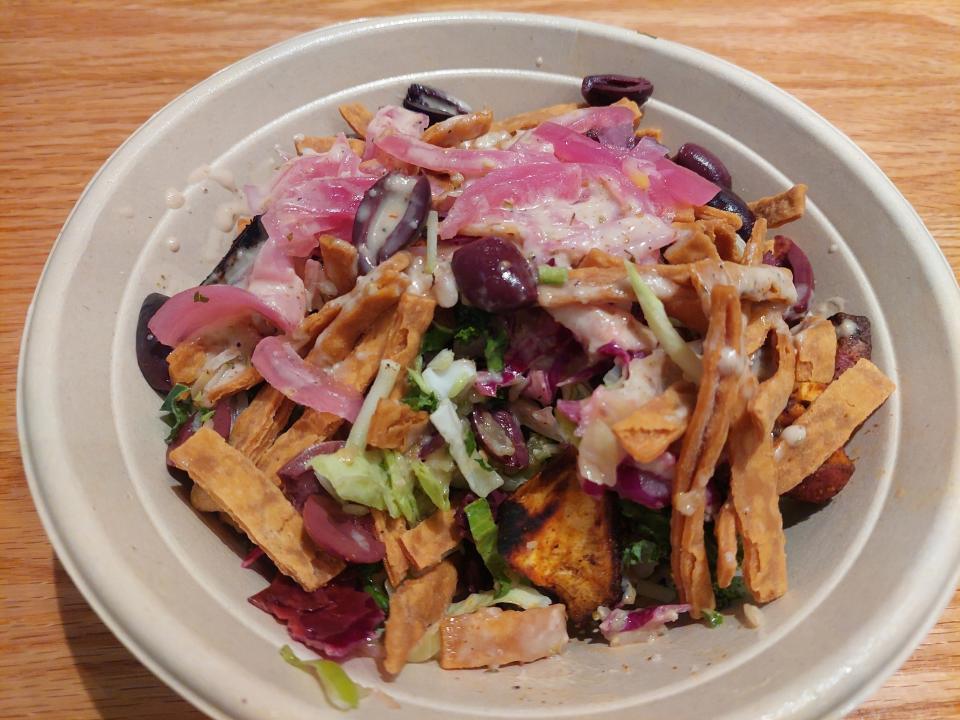 A bowl containing tortilla chips, pink onion, black olives, sauce and salad from the Cava restaurant in Chicago