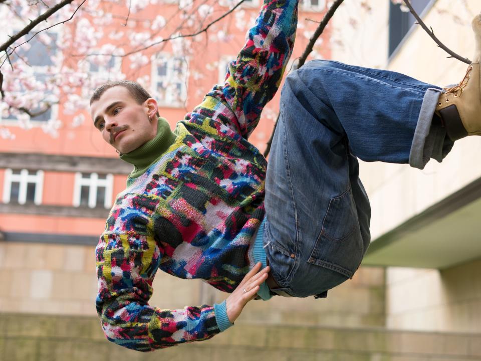 A man climbs a wall wearing a vibrant sweater and blue jeans