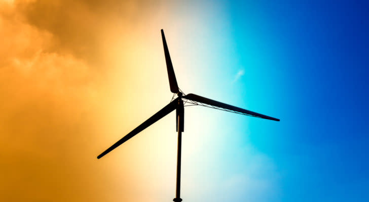 A wind turbine appears in silhouette against a bright orange and blue sky.