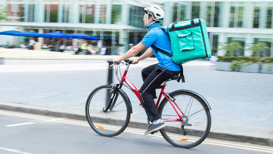 Courier On Bicycle Delivering Food In City.