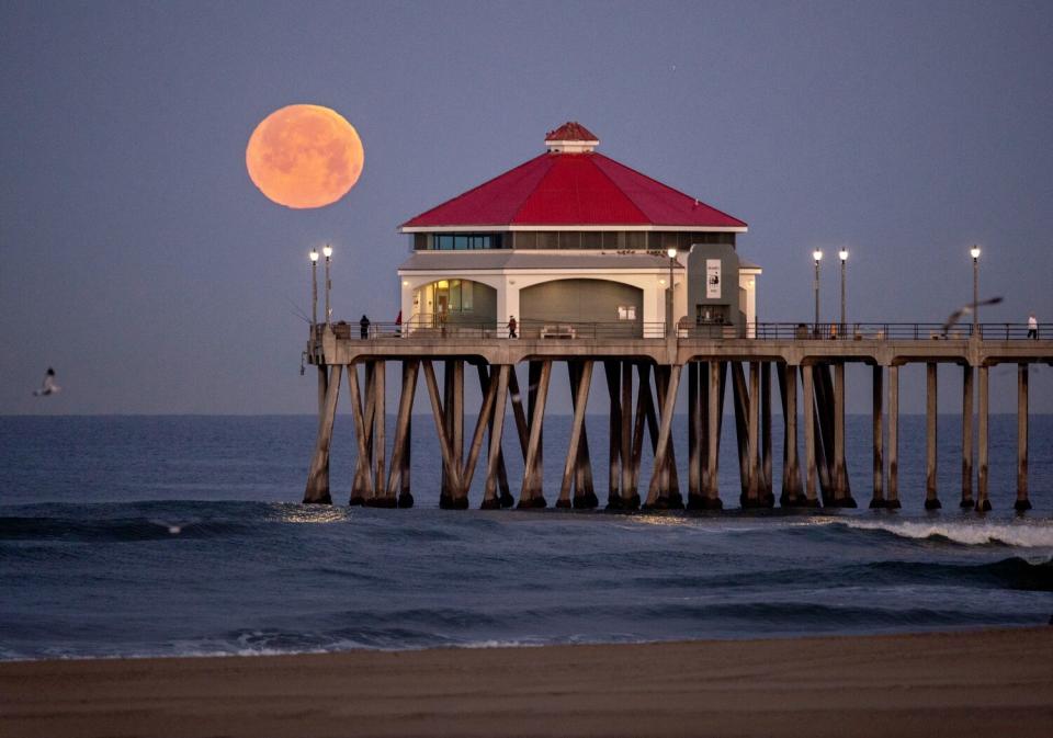 A full pink moon raises behind the Huntington Beach Pier