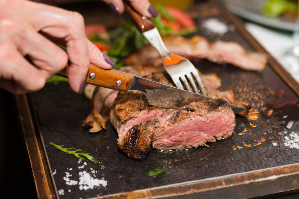 Woman hand holding knife and fork cutting grilled beef steak.