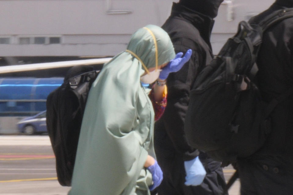 In this image taken from a video, Silvia Romano is flanked by two masked security officers as she walks on the tarmac after landing at Rome's Ciampino airport, Sunday, May 10, 2020. Wearing a surgical mask, disposable gloves and booties to guard against COVID-19, a young Italian woman has returned to her homeland after 18 months as a hostage in eastern Africa. (AP Photo/Paolo Santalucia)