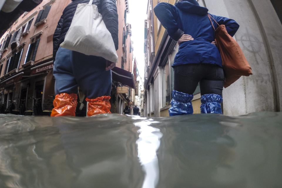 People wade their way through water in Venice, Italy, Friday, Nov. 15, 2019. Exceptionally high tidal waters returned to Venice on Friday, prompting the mayor to close the iconic St. Mark's Square and call for donations to repair the Italian lagoon city just three days after it experienced its worst flooding in 50 years. (AP Photo/Luca Bruno)